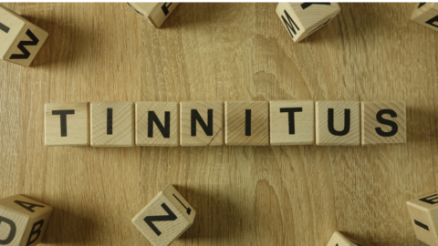 Små träbitar i form av tärningar med bokstäver ligger på ett bord. De är placerade i en rad som formar ordet tinnitus. Runtomkring finns fler träbitar med bokstäver som omger ordet tinnitus.