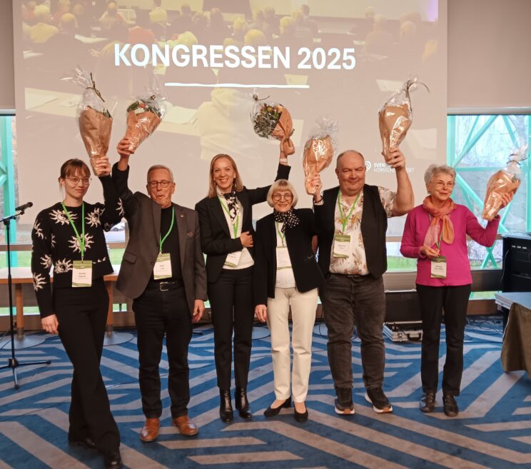 De sex nyvalda styrelsemedlemmarna poserar tillsammans framför kameran. De ler glatt och håller upp blombuketter i luften,