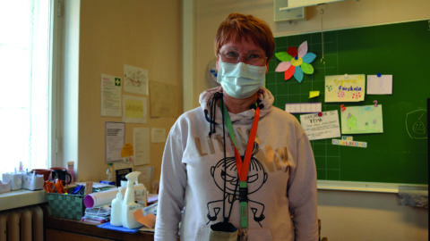 Förskolelärare Maria Eriksson står i sitt klassrum framför sitt skrivbord. Bakom skrivbordet finns en tavla ed olika lappar och papper uppsatta.