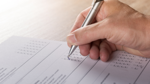 En blankett på ett bord fylls i av en hand som hpller i en kulspetspenna.