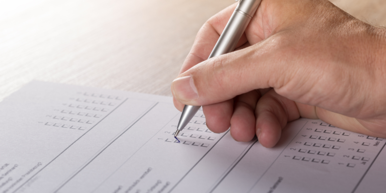 En blankett på ett bord fylls i av en hand som hpller i en kulspetspenna.