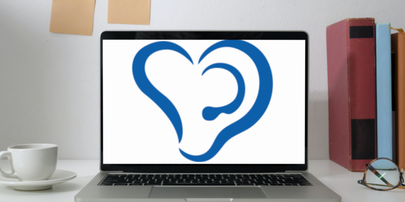 En laptop står på ett skrivbord. På vänster sida finns en kaffekopp och på högra sidan står tre böcker. På bordet ligger ett par glasögon. I laptopens skärm syns Svenska hörselförbundets logo. Logon ser ut som två öron som formar ett hjärta.