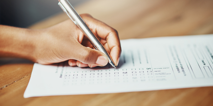 På bilden finns en vänsterhand som håller i en kulspetspenna och fyller i en blankett genom att sätta kryss i rutor.