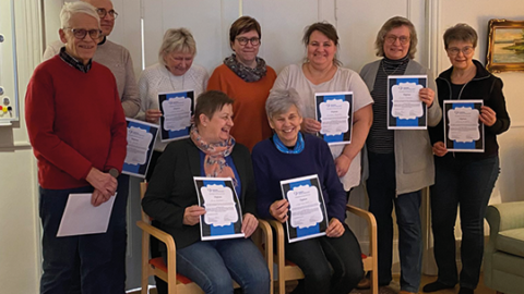 En grupp med män och kvinnor poserar för gemensam bild. Personerna ler mot kameran och håller i ett diplom.