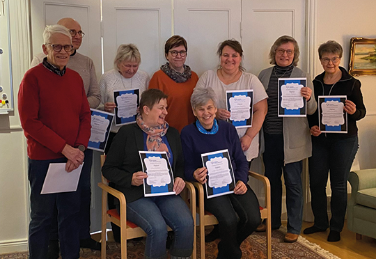 En grupp med män och kvinnor poserar för gemensam bild. Personerna ler mot kameran och håller i ett diplom.