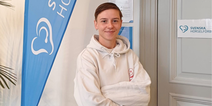 Emmy Nyström poserar framför förbundets reklamflagga. Emmy har armarna i kors och ler mot kameran.